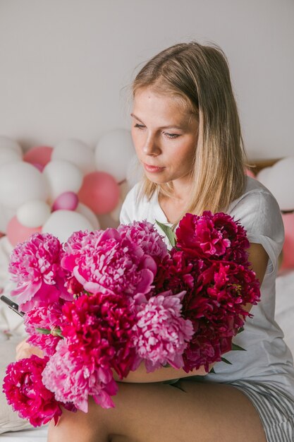 Afbeelding van een gelukkige positieve mooie jonge vrouw binnenshuis thuis in de slaapkamer in bed met bloemen en maak een selfie via de mobiele telefoon.