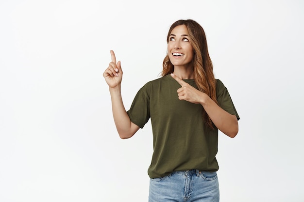 Afbeelding van een gelukkige volwassen vrouw, een vrouwelijk model dat kijkt en wijst naar de linkerbovenhoek met een lachend hoopvol gezicht, een goede kans ziet, staande tegen een witte achtergrond.