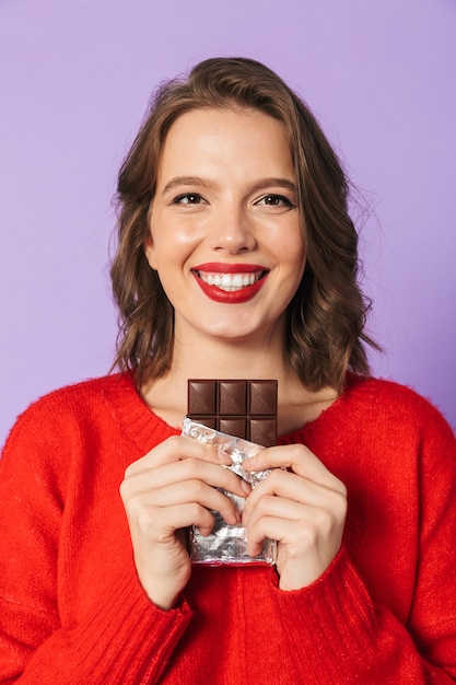 Afbeelding van een geschokt emotionele jonge vrouw poseren geïsoleerd over paarse muur muur met chocolade.