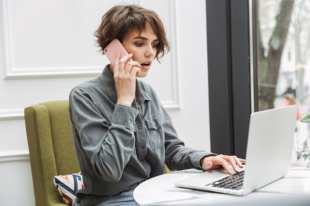 Afbeelding van een geschokte emotionele verraste jonge, mooie zakenstudentvrouw die binnenshuis in café zit met behulp van laptopcomputer coworking.