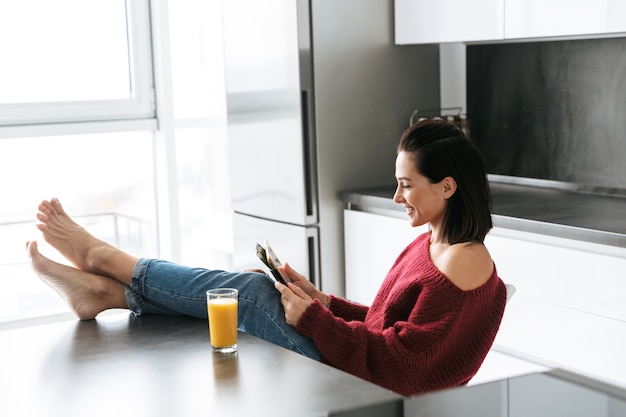 Afbeelding van een geweldige vrouw binnenshuis in huis in de keuken met behulp van tabletcomputer.