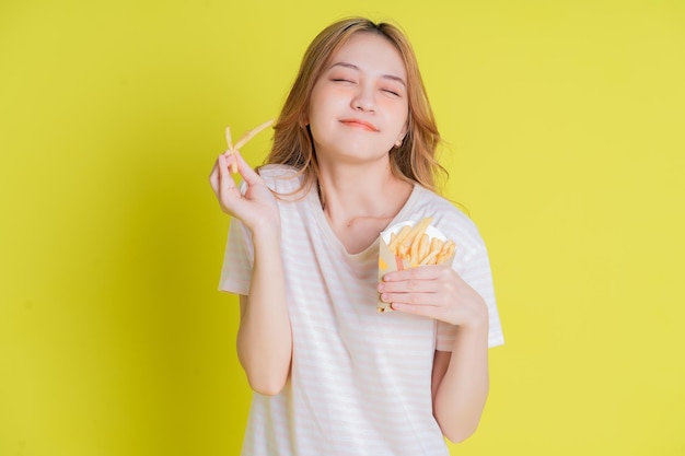 Afbeelding van een jong Aziatisch meisje dat frietjes eet op gele achtergrond