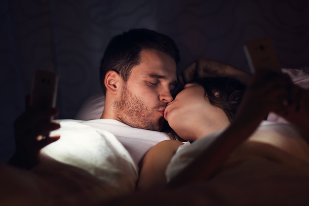 Afbeelding van een jong stel dat 's nachts smartphones in bed gebruikt