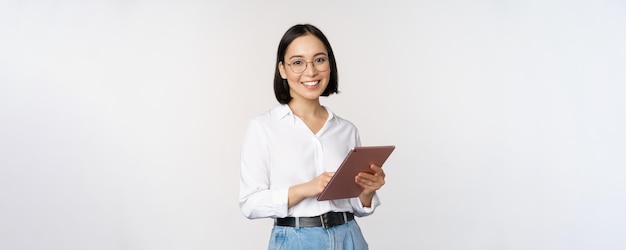 Afbeelding van een jonge Aziatische vrouw die een bedrijfsmedewerker in een bril glimlacht en een digitale tablet vasthoudt die op een witte achtergrond staat