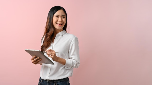 Afbeelding van een jonge Aziatische vrouw die een tablet vasthoudt terwijl ze met een roze geïsoleerde achtergrond staat