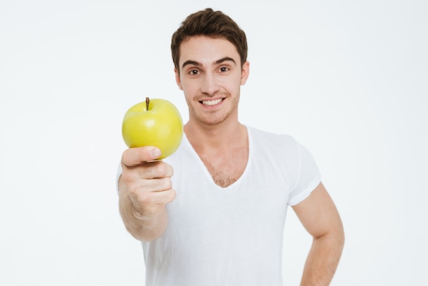 Afbeelding van een jonge gelukkige man gekleed in een wit t-shirt dat over een witte achtergrond staat en een appel vasthoudt.