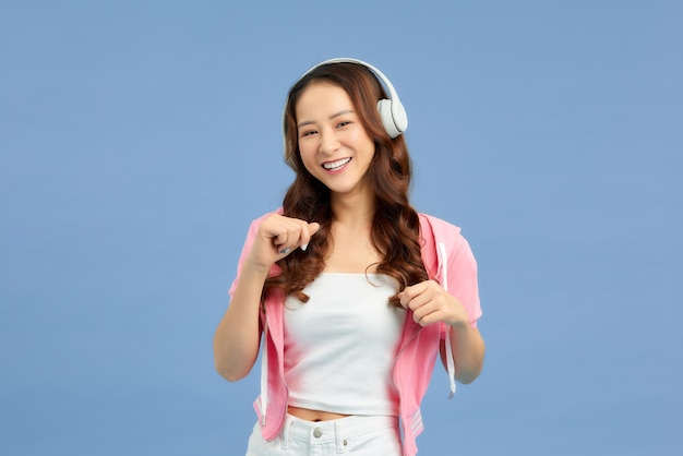 Afbeelding van een jonge, mooie vrouw die geïsoleerd staat over een achtergrond met kleur die muziek luistert met een koptelefoon