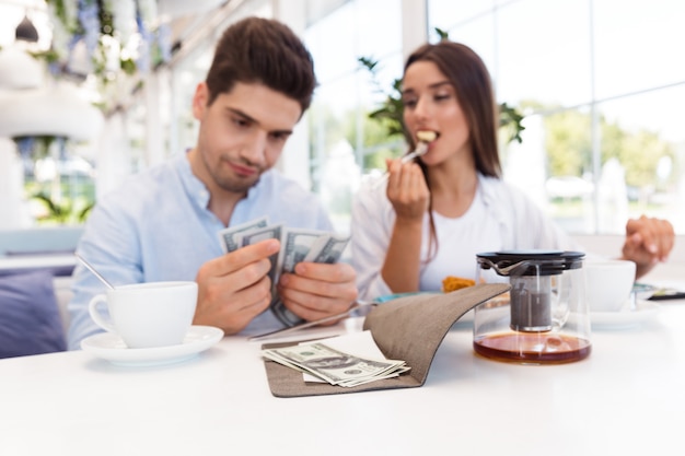 Afbeelding van een jonge ontevreden verward verliefde paar zitten in de cheque en geld van de caféholding.