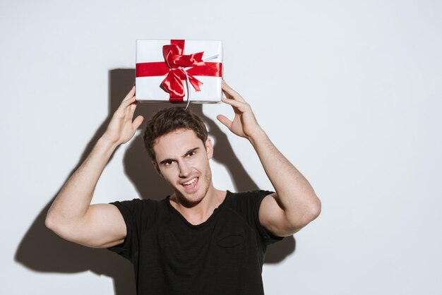 Afbeelding van een jonge schreeuwende man gekleed in een zwart t-shirt dat over een witte achtergrond staat met een cadeau.