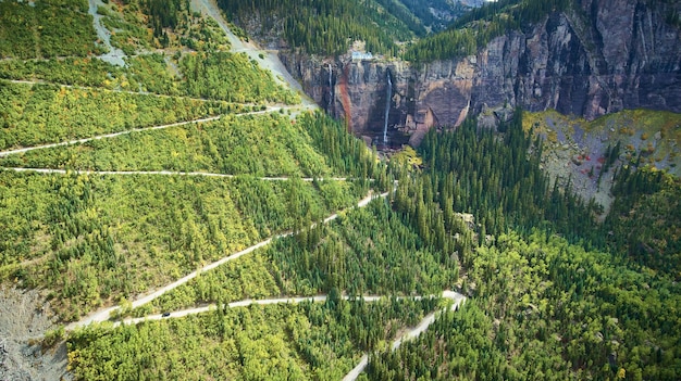 Afbeelding van een kleine onverharde weg die zigzaggend een grote bergwand oploopt naar watervallen op kliffen