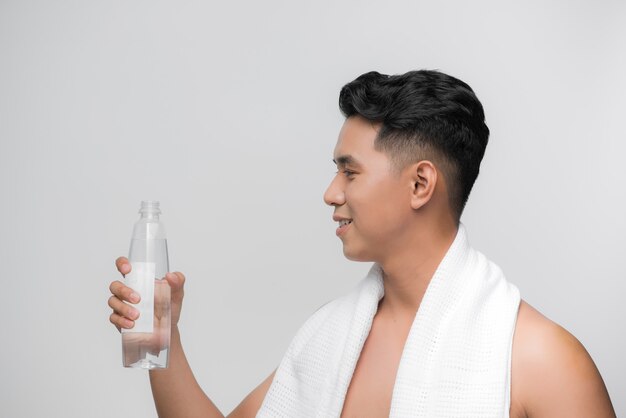 Afbeelding van een knappe glimlachende man met een witte handdoek op zijn schouders die een fles water vasthoudt na de training op een witte achtergrond