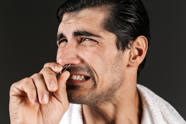 Afbeelding van een knappe jongeman poseren geïsoleerd haar ontharen uit de neus met een pincet.