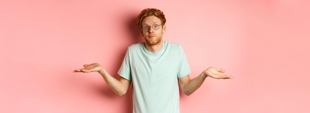 Foto afbeelding van een knappe roodharige man in een bril en een t-shirt die niets weet, schouders opheft en een persoon opheft.