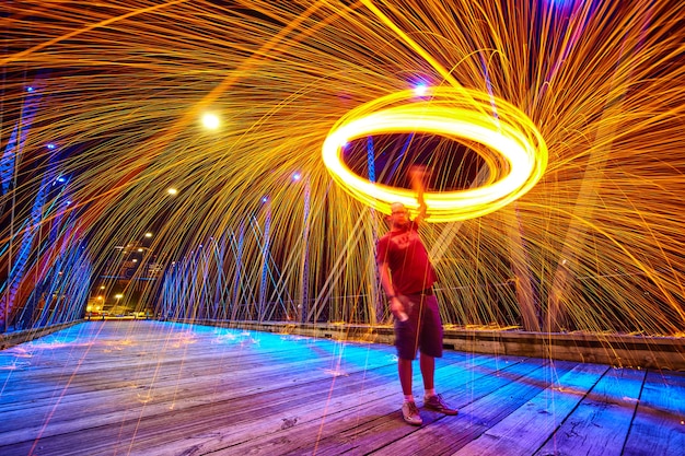 Afbeelding van een man die 's nachts een lasso van gele vonken en licht op een brug draait