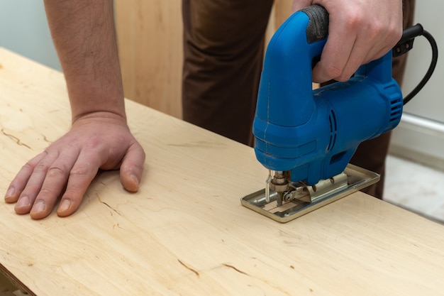 Afbeelding van een man hand met behulp van elektrische decoupeerzaag. close-up proces van houten plank snijden.