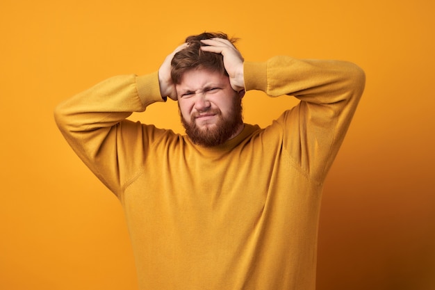 Afbeelding van een man in basiskleding, close-up van ongelukkig knappe man met baard haar met handen vast te houden