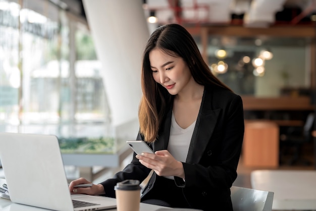 Afbeelding van een mooie aziatische zakenvrouw die een smartphone vasthoudt en een laptop gebruikt in een café.