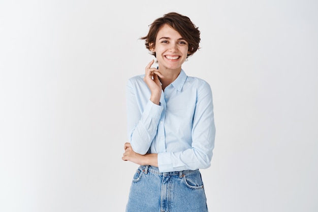 Afbeelding van een mooie blanke vrouw in een blauw shirt die lacht, er gelukkig uitziet, op een witte muur staat