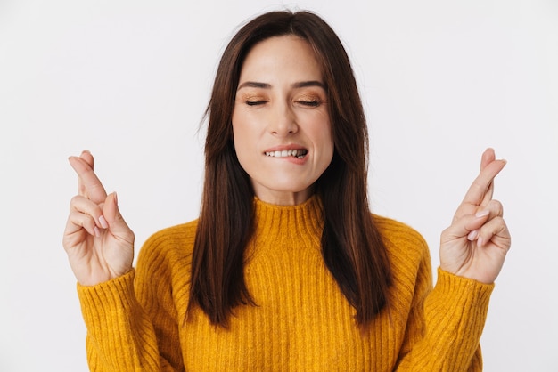 Afbeelding van een mooie brunette volwassen vrouw die een trui draagt die vingers gekruist houdt voor geluk geïsoleerd op wit