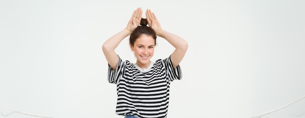 Foto afbeelding van een mooie, gelukkige jonge vrouw die konijnenoren bovenop haar hoofd toont en er opgewonden uitziet