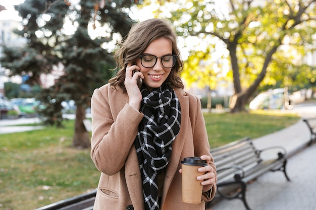 Afbeelding van een mooie gelukkige jonge vrouw praten via de mobiele telefoon buitenshuis wandelen door de straat.