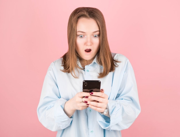 Afbeelding van een mooie geschokt jonge brunette die zich voordeed op een roze muur met behulp van een mobiele telefoon.