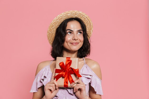 Afbeelding van een mooie jonge gelukkige vrouw poseren geïsoleerd over roze muur met huidige geschenkdoos.