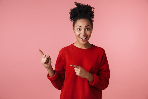 Afbeelding van een mooie jonge opgewonden gelukkige emotionele Afrikaanse vrouw die zich voordeed over het roze muur wijzen.