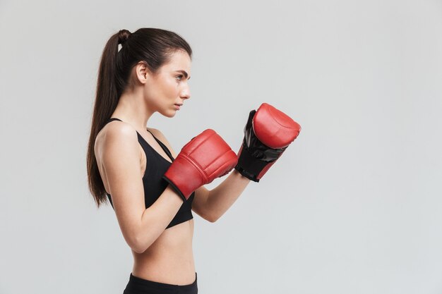 Afbeelding van een mooie jonge sport fitness vrouw bokser geïsoleerd over grijze muur maken oefeningen in handschoenen.