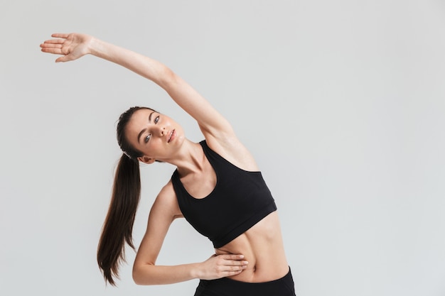 Afbeelding van een mooie jonge sport fitness vrouw maken oefeningen geïsoleerd over grijze muur.