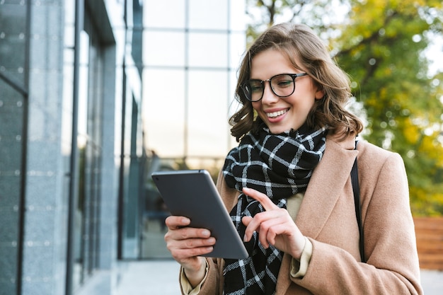 Afbeelding van een mooie jonge vrouw buiten wandelen door straat met behulp van tablet-computer.