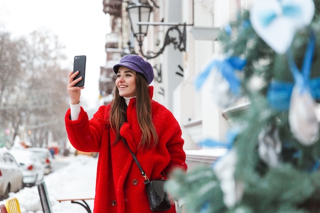 Afbeelding van een mooie jonge vrouw buiten wandelen op straat sneeuw winter nemen selfie via mobiele telefoon.