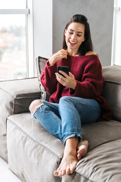 Afbeelding van een mooie vrouw binnenshuis in huis op de bank met behulp van mobiele telefoon.