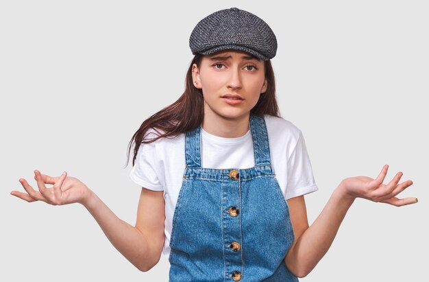 Afbeelding van een ondervraagde jonge vrouw die er serieus uitziet, gekleed in een casual trendy outfit die over een witte muur poseert Studentmeisje heeft een verwarde uitdrukking Mensenemoties