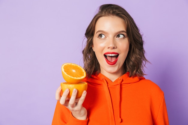 Afbeelding van een opgewonden mooie jonge vrouw poseren geïsoleerd over paarse muur muur met oranje citrus.