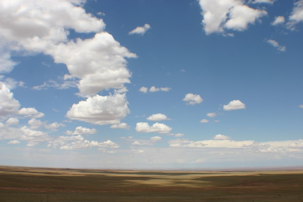 Afbeelding van een panoramische opname van de blauwe lucht van New Mexico met verspreide wolken boven de vlakke woestijngrond