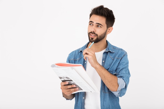 Afbeelding van een serieuze bebaarde man die in een werkboek schrijft terwijl hij opzij kijkt, geïsoleerd over een witte muur