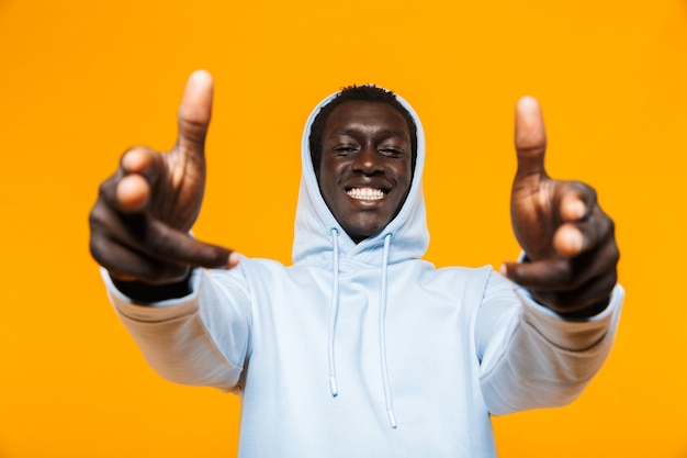 Afbeelding van een tevreden Afro-Amerikaanse man in streetwear hoodie die lacht en met de vingers naar je wijst