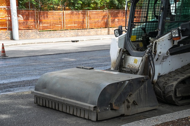 Afbeelding van een tractor met een asfalteermachine voor wegwerkzaamheden in stedelijke omgeving