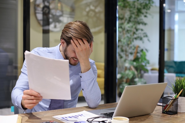 Afbeelding van een vermoeide jonge zakenman in pak die zijn gezicht in handen houdt terwijl hij op kantoor zit