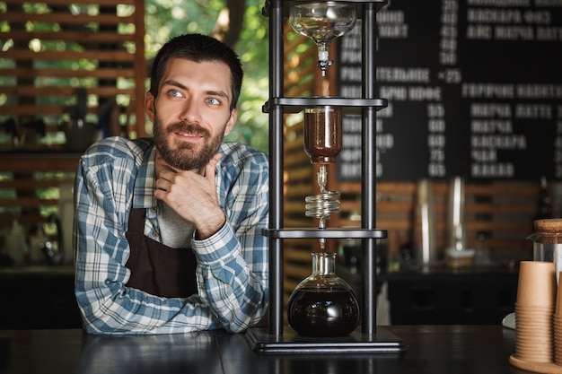 Afbeelding van een vrolijke barista-jongen met een schort die koffie maakt terwijl hij in een café of koffiehuis buiten werkt