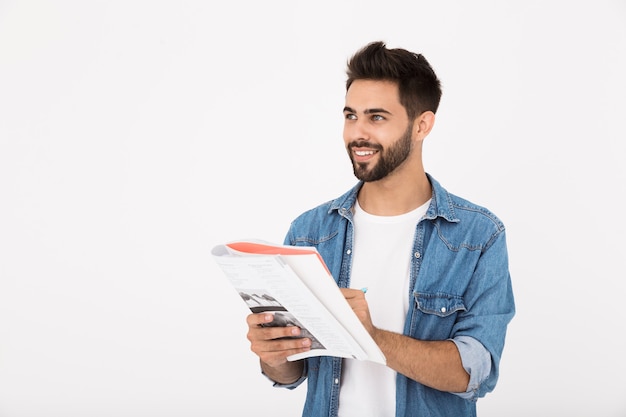 Afbeelding van een vrolijke, bebaarde man die in een werkboek schrijft en glimlacht terwijl hij opzij kijkt, geïsoleerd over een witte muur