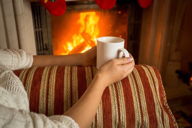 Afbeelding van een vrouw die op de bank bij de open haard zit en een kopje thee vasthoudt