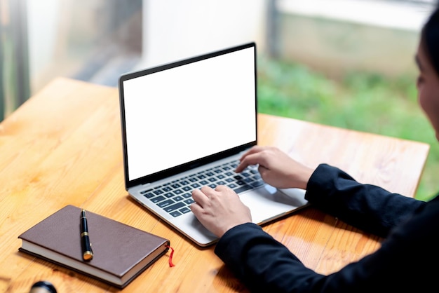 Afbeelding van een zakenvrouw die werkt met een laptop toetsenbord leeg wit scherm met notebook en pen op bureau. Bespotten.