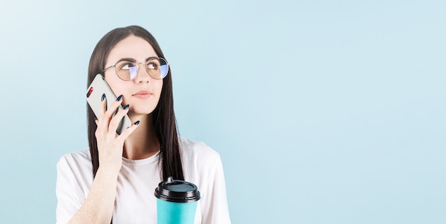 Afbeelding van gelukkige Amerikaanse vrouw die en vriend glimlacht belt terwijl het drinken van koffie die over blauwe muur met copyspace wordt geïsoleerd