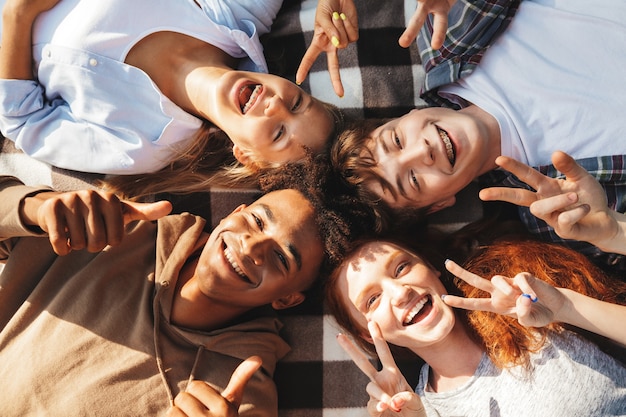Afbeelding van gelukkige jonge vrienden, mannen en vrouwen die lachen en op een deken in een cirkel liggen