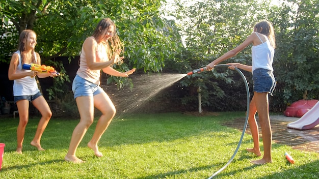 Afbeelding van gelukkige kinderen die in de achtertuin van het huis spelen met waterpistolen en tuinslang. Familie spelen en plezier hebben buiten in de zomer