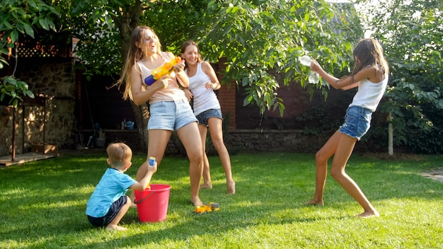 Afbeelding van gelukkige vrolijke familie spelen in de achtertuin. Mensen opspattend water met waterpistolen en tuinslang.