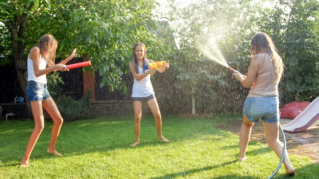 Afbeelding van gelukkige vrolijke familie spelen in de achtertuin. Mensen opspattend water met waterpistolen en tuinslang.