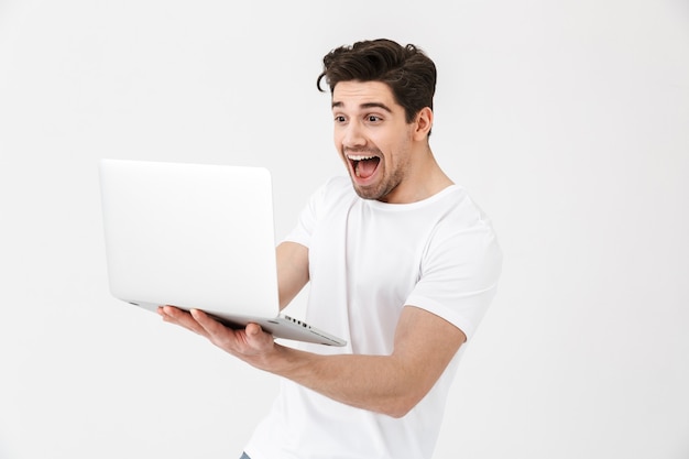 Afbeelding van geschokt opgewonden jonge man poseren geïsoleerd over witte muur met behulp van laptopcomputer.
